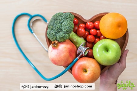 گوشی پزشکی به همراه ظرف چوبی شبیه قلب که در آن سبزیجات و میوه های تازه است و تاثیر گیاهخواری در سلامت قلب و عروق
